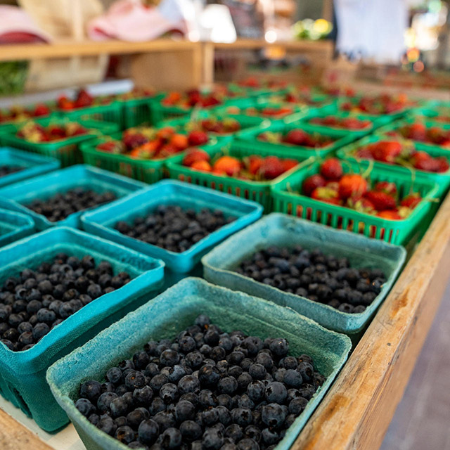 Small square baskets of blueberries and strawberries are arranged in rows on a table at a farmer’s market.