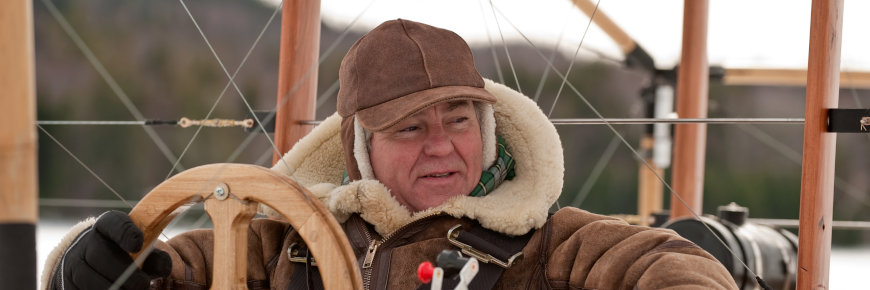 A man sitting at the controls of a wooden flying machine.