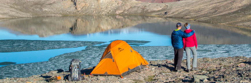 Two people standing by a tent in an arctic landscape.