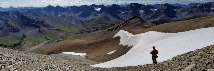 A man standing beside a patch of ice in a mountain landscape.