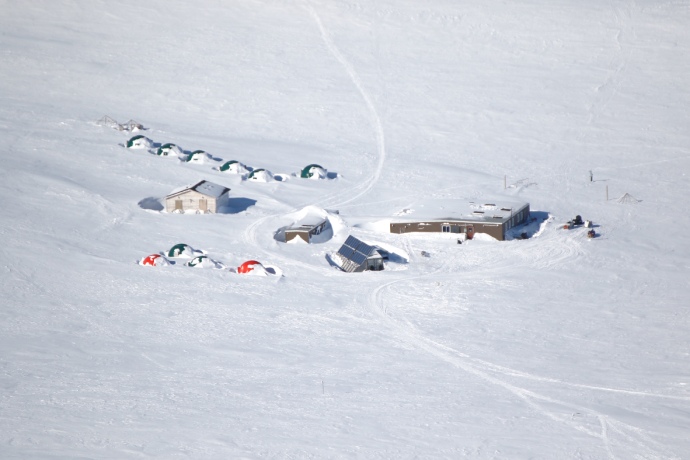 An aerial view of the wintry base camp with some structures half covered in snow drifts.