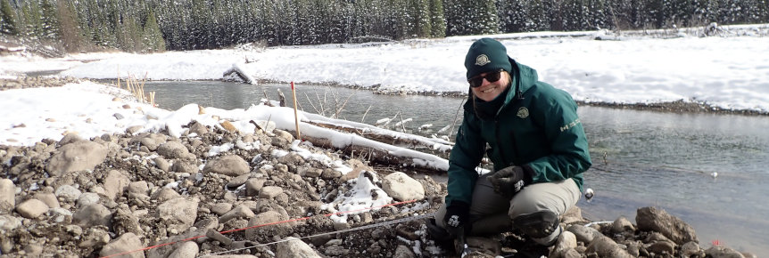 A Parks Canada staff member kneeling in front of a creek.