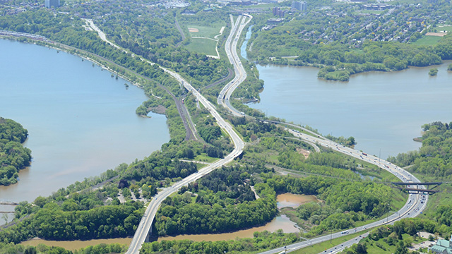 Aerial view of a narrow strip of wooded land bordered by water and crossed by roads and highways connecting urbanized areas