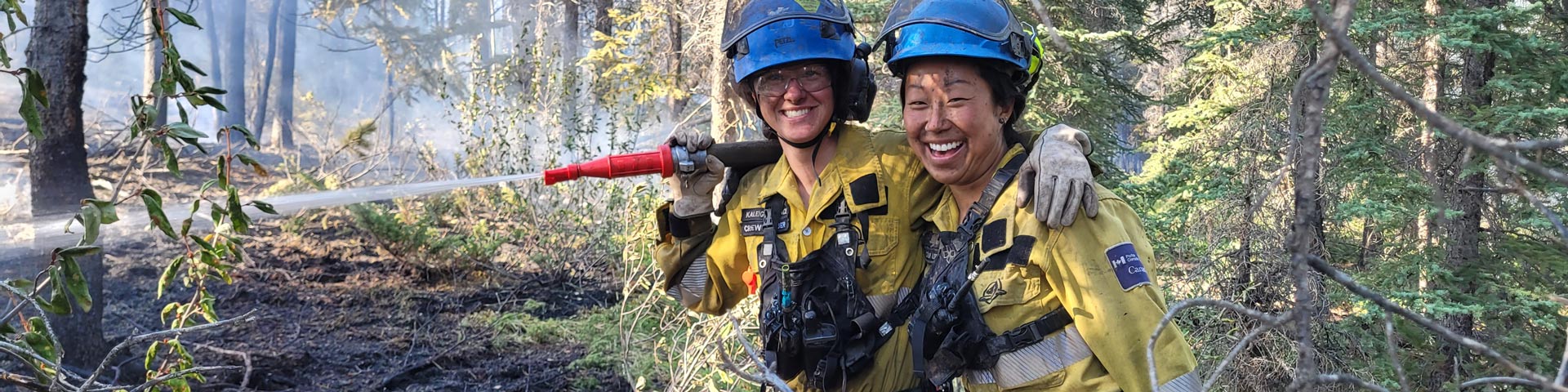 Two fire crew members smile for the camera while holding a fire hose during the Chetamon Wildfire in Jasper National Park