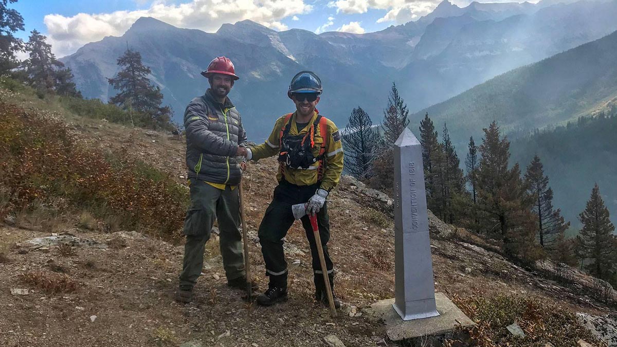 Des pompiers de Parcs Canada et du United States National Park Service se serrent la main de l’autre côté de la frontière internationale dans le parc national des Lacs Waterton.