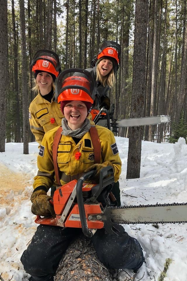 Three fire crew members pose for the camera while holding chainsaws during wildfire risk reduction work in Banff National Park