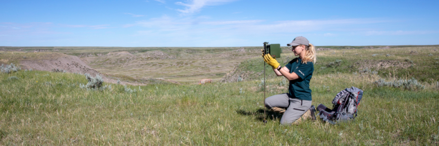 Woman beside a camera with a prairie landscape behind.