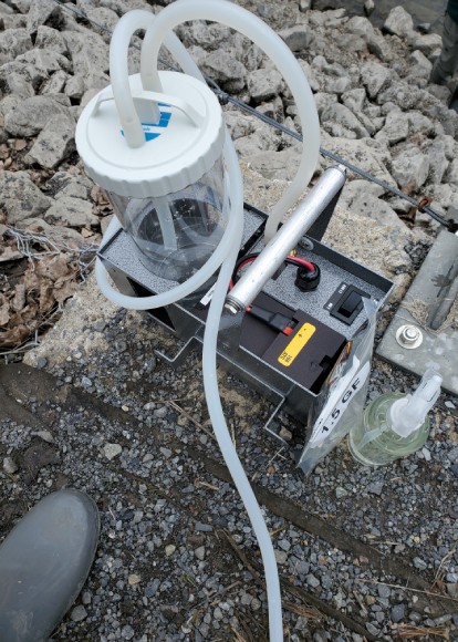 A close up of a small device on the ground with a container and tubing attached to it.