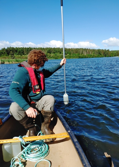 A Parks Canada employee sits in a canoe while using a long pole to take water samples.