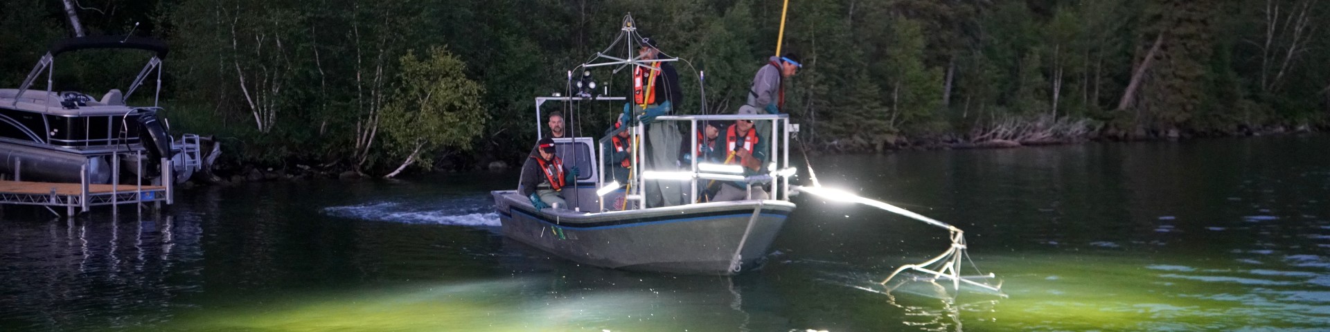 Les membres de l’équipage d’un bateau de pêche électrique à la tombée de la nuit illuminent le lac en faisant glisser les engins suspendus dans l’eau.