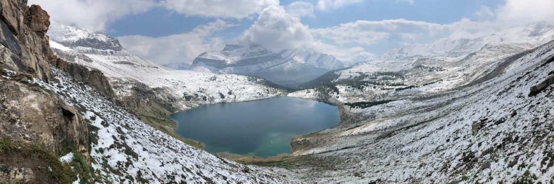 Une vue d’un grand lac situé loin sur les contreforts d’une montagne enneigée qui l’entoure.