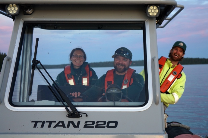 Three Parks Canada staff members peer out the window of their ship’s wheelhouse while on a lake.