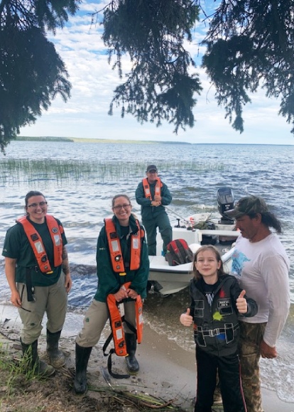 Quatre adultes et un enfant sourient à l’appareil-photo devant un bateau sur le rivage.