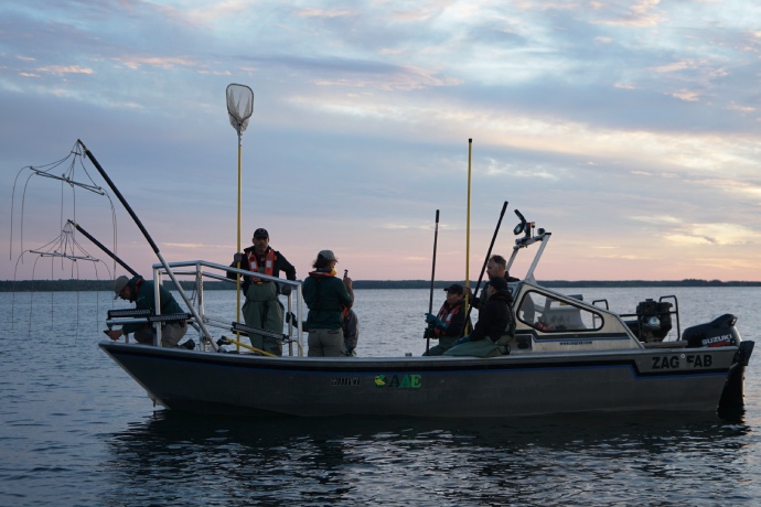 Sept membres d’équipage et divers équipements à bord d’un bateau de pêche électrique au crépuscule.