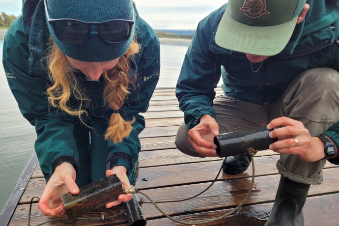 Two Parks Canada staff members crouch down on a dock to carefully inspect a cabled device.