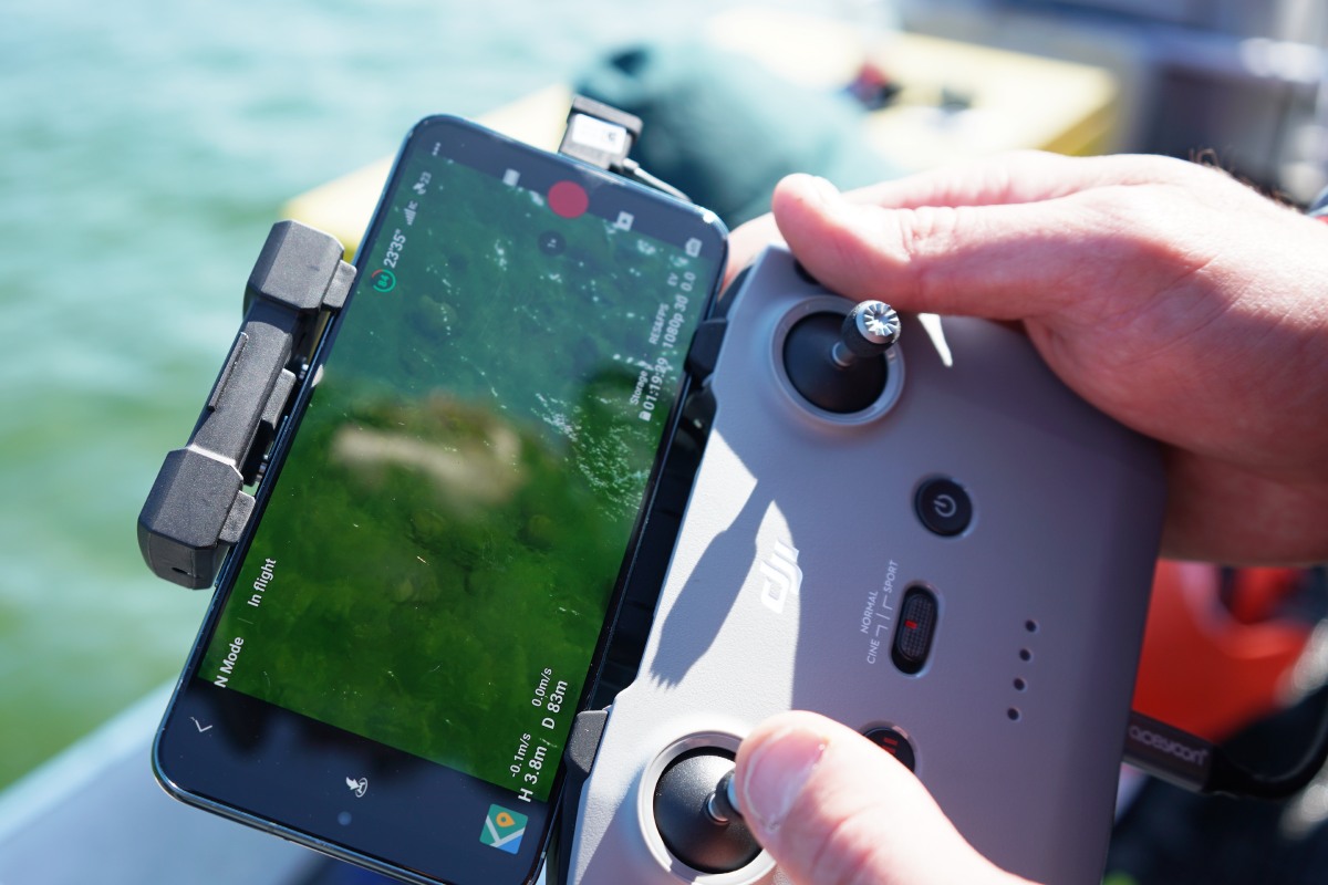 Gros plan d’une personne manipulant l’écran de contrôle d’un drone sur un bateau.