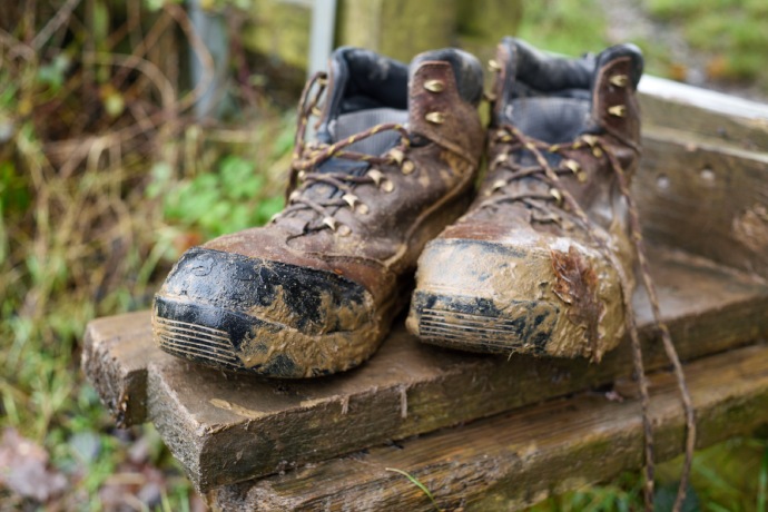 A close up of a pair of boots covered in mud and plant debris.