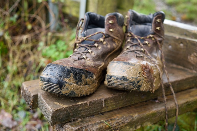 Gros plan sur une paire de bottes couvertes de boue et de débris végétaux.