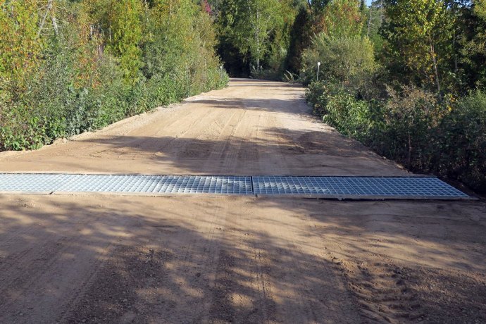 A dirt road has a narrow metal grate running from one side to the other.
