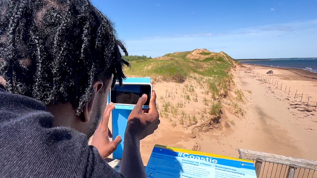 A person leans in toward a Coastie station to take a photo of the sandy coastline of a beach.