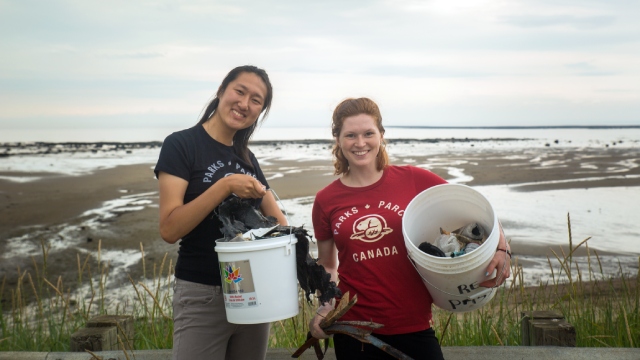 Two smiling participants proudly show the waste they have collected in plastic buckets.