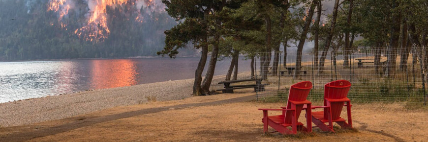 two red chairs at a lakeside with a burning forest in the background