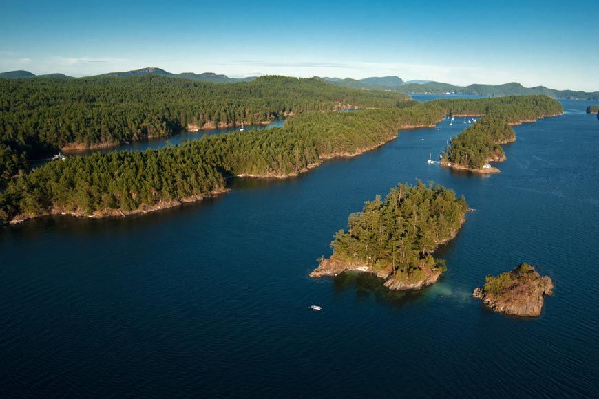 Une vue aérienne d’îles couvertes de forêts et de collines vallonnées entourées d’une eau bleue et sous un ciel bleu.