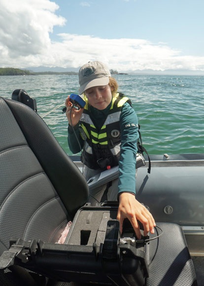 Une employée de Parcs Canada à bord d’un bateau sur l’eau écoute un appareil qui l’aide à entendre les bruits sous-marins.