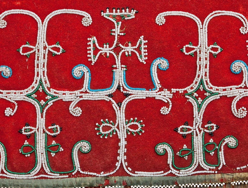 Intricate Mi’kmaq beadwork. White beads on a red cloth background.