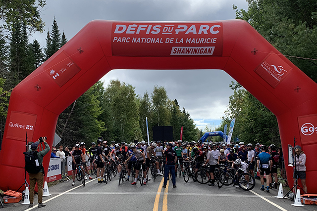Several cyclists starting their bike race at the Défis du Parc passing under the start/finish arch.