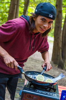 A youth cooks a fish outdoors.