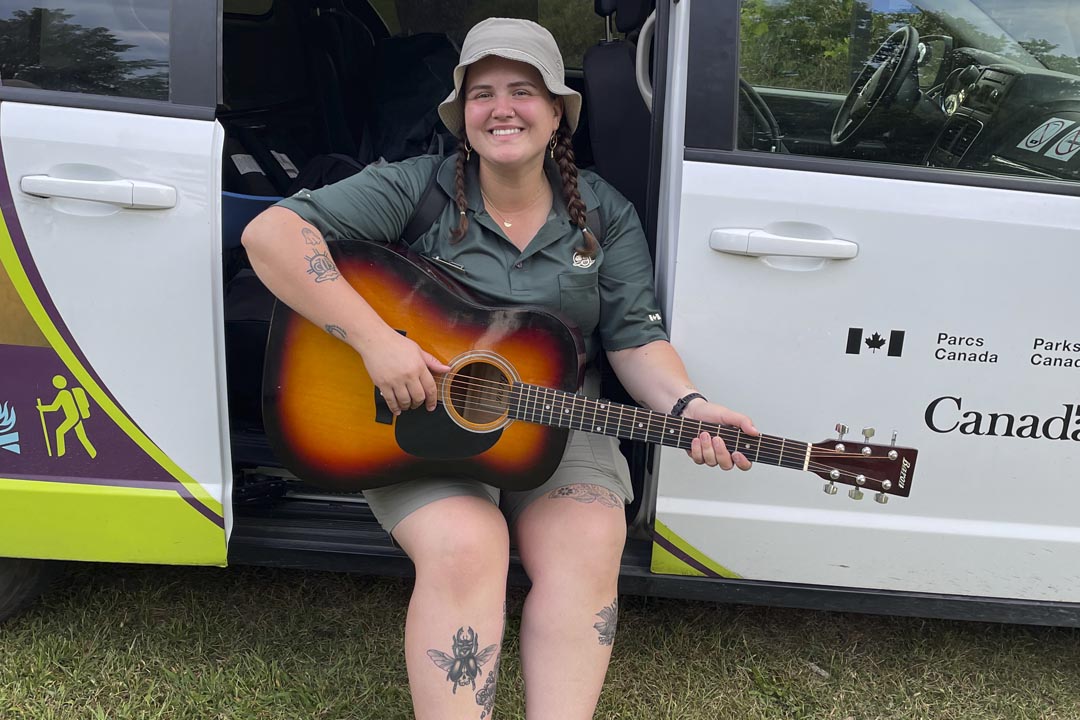 Tierney joue de la guitare assis dans la camionnette Learn-to Camp.
