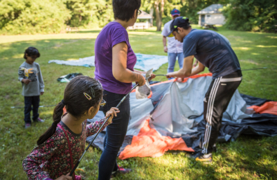 Trois adultes et un enfant travaillent ensemble pour monter une tente sur le gazon.