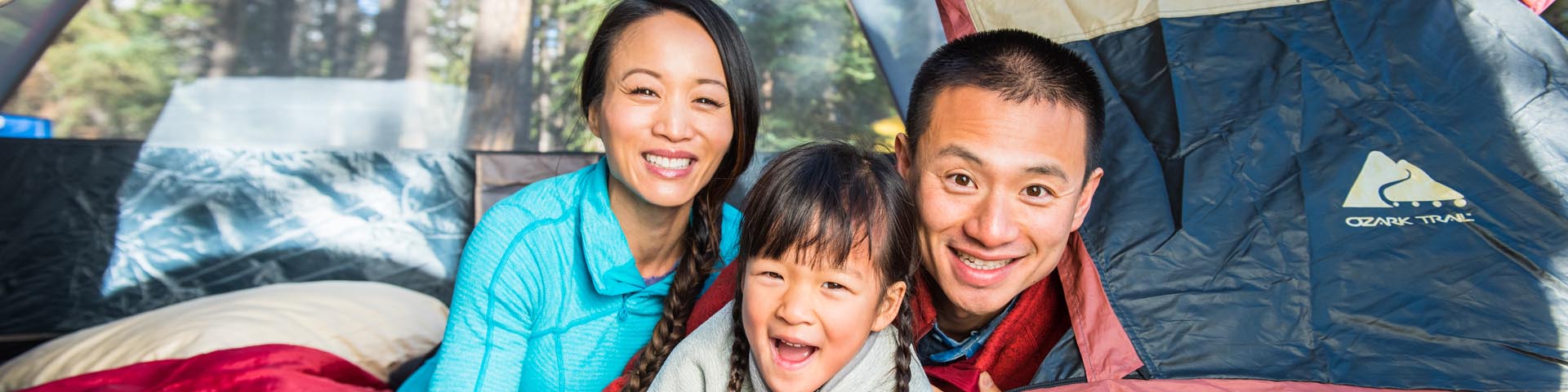 A family smiles while looking out from a tent at Two Jack Lakeside Campground on a fall morning. 