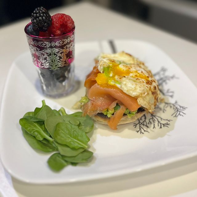 The assembled brunch sandwich on a plate with spinach and a cup of berries on the side.