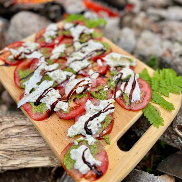 A plate of red heirloom tomatoes topped with torn burrata, pesto, and a drizzle of balsamic reduction.