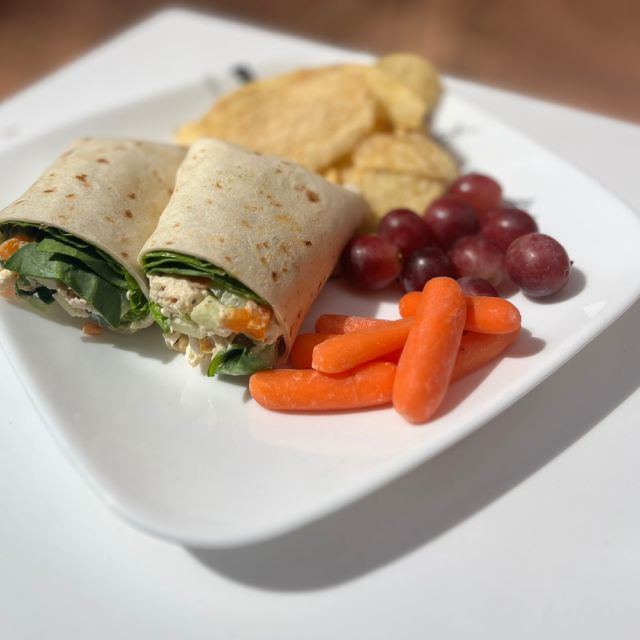 Halved tortilla wraps on a plate served with carrots, grapes, and chips.