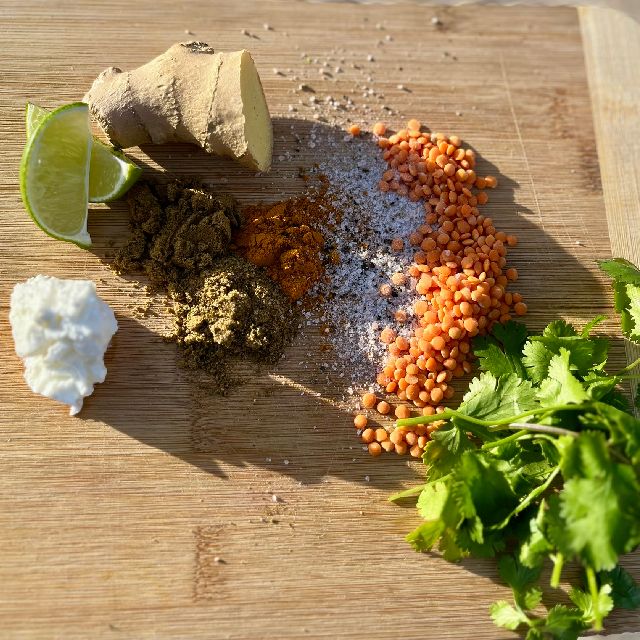 Ingredients  arranged on a cutting board, including spices, cilantro, fresh ginger, and lentils.