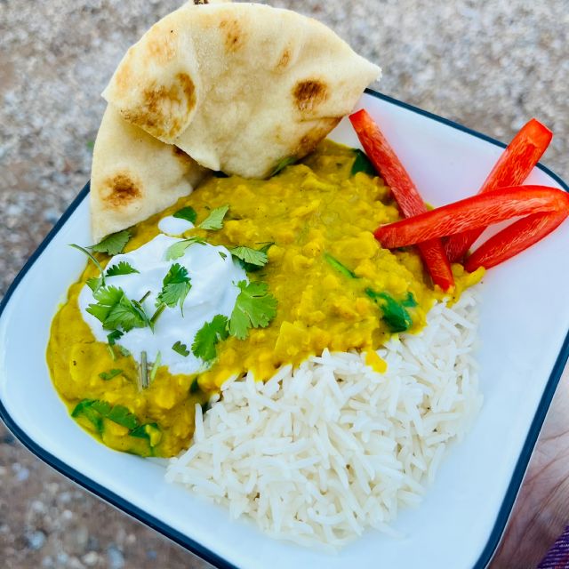 Finished dahl in a bowl served with rice, naan, and red bell pepper slices, garnished with cilantro and Greek yogurt.