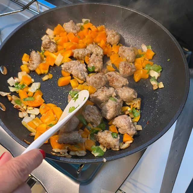  Sliced sausages, onion, and peppers being sautéed in a large pan until lightly browned.