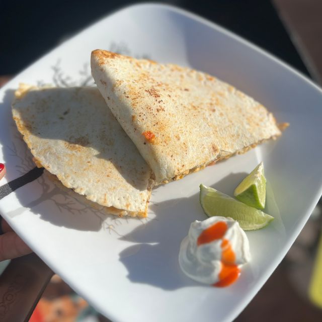 The cooked quesadilla cut in half on a plate, served with lime wedges and sour cream.