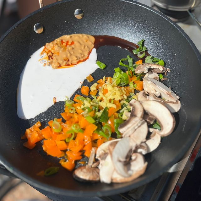  Ingredients for ramen in a pan before cooking, including green onion, mushrooms, ginger, coconut milk, and peanut butter.