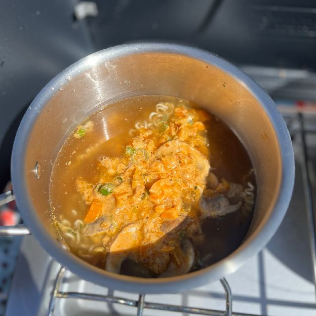 A pot of broth cooking over a camp stove.