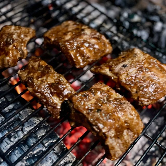 Ribs cooking on a grill placed over hot campfire embers.