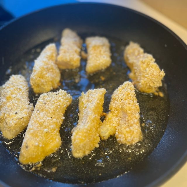 A skillet of hot oil frying several pieces of coated white fish until golden and crispy.