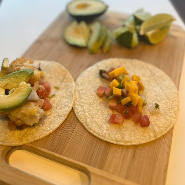 Tacos filled with toppings on a cutting board with lime wedges and avocado slices.
