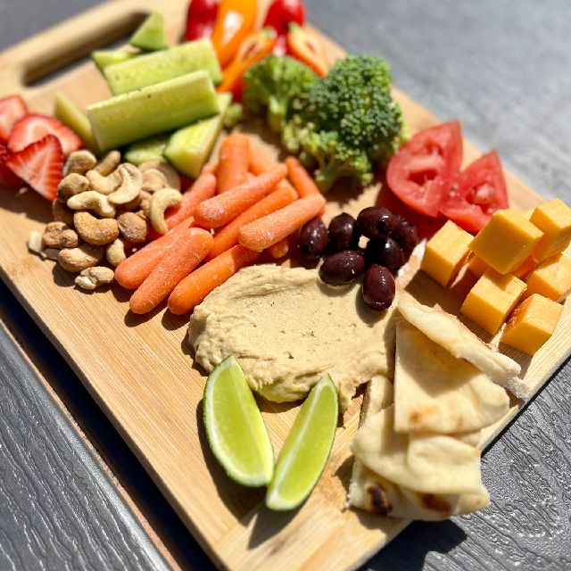 A platter with an assortment of fresh vegetables, mini pitas, cheese, and hummus.