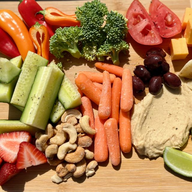 A platter with an assortment of fresh vegetables, mini pitas, cheese, and hummus.