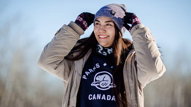 A young woman smiles into the distance and adjusts her toque while wearing her official merchandise.