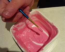 A hand holding a paint brush and a bowl filled with pink melted chocolate